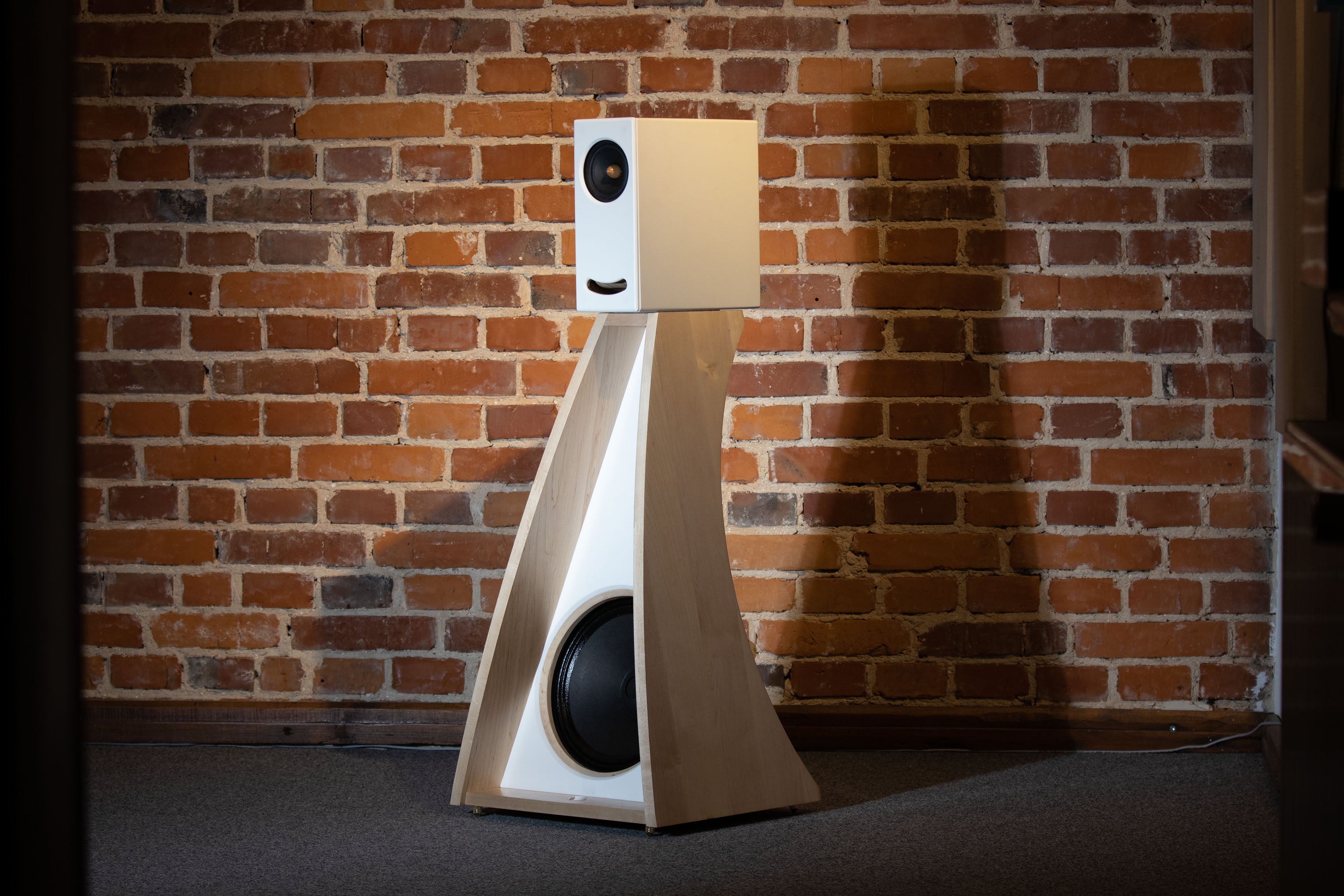 Front view of the Closer Acoustics The Full OGY Loudspeaker Set – Pair in solid maple finish, placed against a brick wall, highlighting the contrast of the natural wood finish and textured backdrop