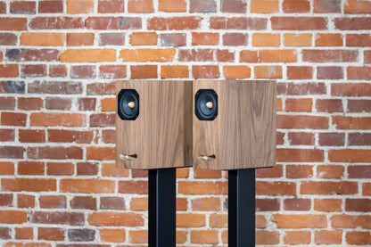 Closer Acoustics OGY bookshelf loudspeakers – pair in walnut veneer, positioned on black stands, showcasing the elegant look in a modern audio setup