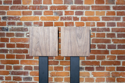 Closer Acoustics OGY bookshelf loudspeakers – pair in walnut veneer, side profile view against a brick wall, emphasizing their stylish design and audio precision in a modern interior